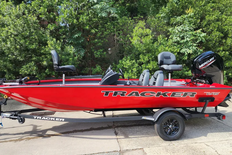 The Image of 2026 Tracker Pro Team 175 boat in vibrant red, parked on a trailer, surrounded by greenery. - 0