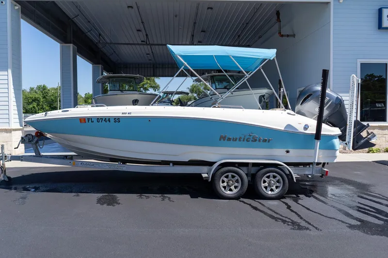 The Image of 2020 NauticStar 203 SC boat on trailer with blue canopy, parked outdoors. - 0