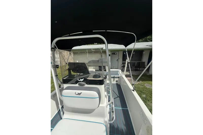 Slide: The Image of 2015 Mako 19 CPX boat interior with console and seating, parked near a house. - 2