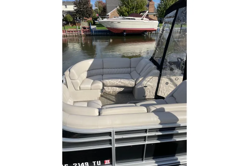 Slide: The Image of 2015 Bennington 2575 QSD pontoon boat with beige seating, docked near a waterfront home. - 10