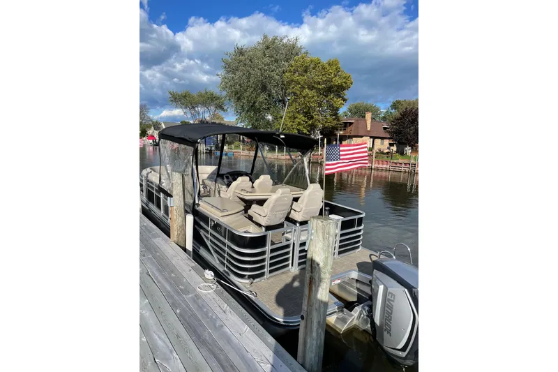 Slide: The Image of 2015 Bennington 2575 QSD pontoon boat docked by a lakeside with American flag. - 11