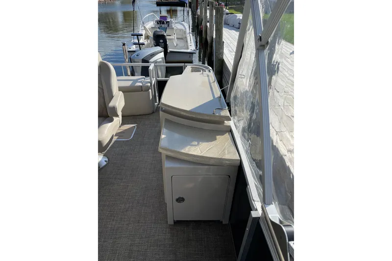 Slide: The Image of 2015 Bennington 2575 QSD boat interior with seating and storage, docked by the water. - 13