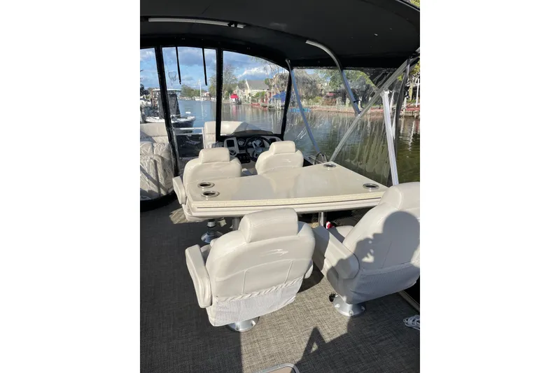 Slide: The Image of 2015 Bennington 2575 QSD boat interior with seating and table, docked by a scenic waterfront. - 14