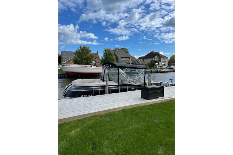 Slide: The Image of 2015 Bennington 2575 QSD pontoon boat docked by waterfront homes under a blue sky. - 16