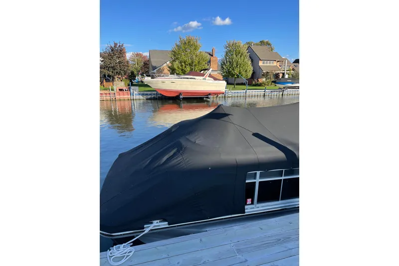 Slide: The Image of Covered 2015 Bennington 2575 QSD boat docked near waterfront homes under clear blue sky. - 8