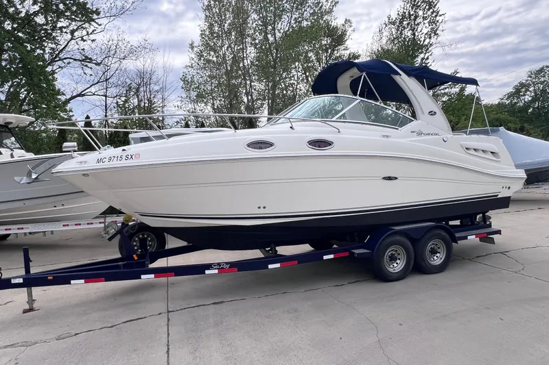 The Image of 2006 Sea Ray Sundancer 260 boat on trailer, parked outdoors with trees in background. - 0