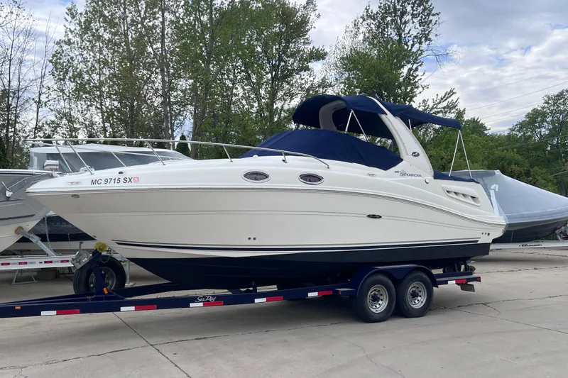 Slide: The Image of 2006 Sea Ray Sundancer 260 boat on trailer, parked outdoors with trees in background. - 1