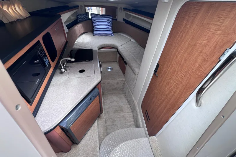 Slide: The Image of 2006 Sea Ray Sundancer 260 cabin interior with kitchenette, seating, and cozy sleeping area. - 13
