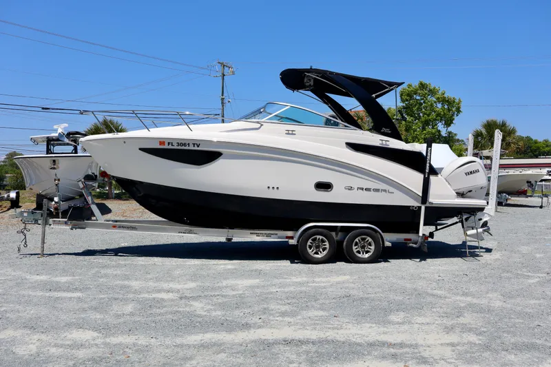 The Image of 2023 Regal 26 XO boat on trailer, parked outdoors under clear blue sky. - 0