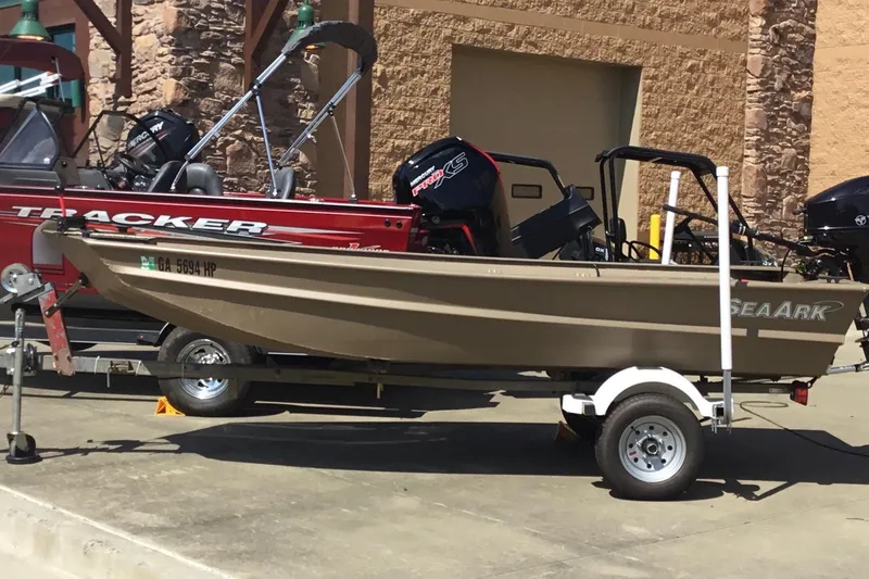 Slide: The Image of 2024 SeaArk 1448 MV boat on trailer, parked beside a Tracker boat. - 5