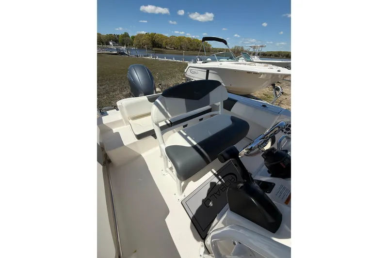 Slide: The Image of 2023 Robalo R202 Explorer boat interior with seating and steering wheel, docked by a lake. - 19