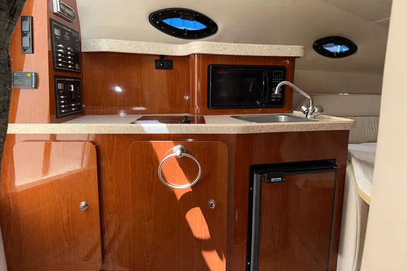 Slide: The Image of 2005 Regal Commodore 2665 boat interior with kitchenette, featuring wood cabinetry and modern appliances. - 25