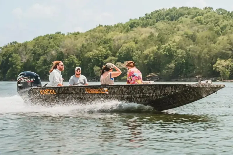 Slide: The Image of Manufacturer Provided Image: 2026 Excel 183 Tomahawk boat cruising on a lake with passengers, surrounded by lush greenery. - 33