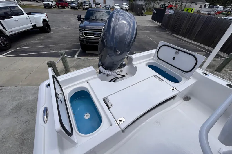 Slide: The Image of 2026 Tidewater 2210 Carolina Bay boat with open storage compartments and motor, parked near vehicles. - 14