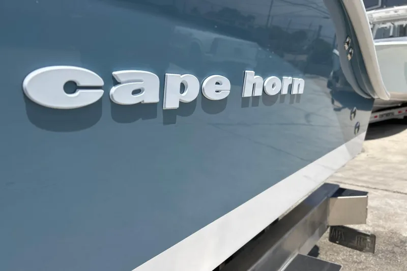 Slide: The Image of 2025 Cape Horn 34 XS boat, close-up of logo on sleek blue hull. - 2