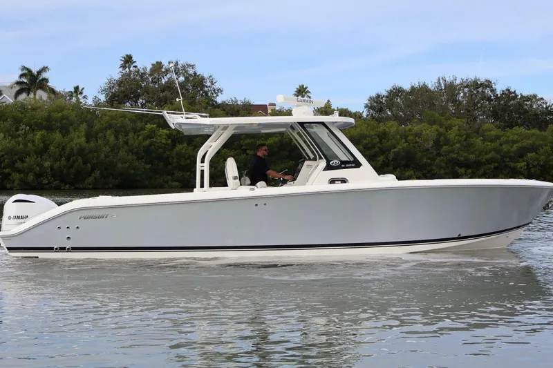 Slide: The Image of 2021 Pursuit S 328 Sport boat cruising on calm water, surrounded by lush greenery. - 2