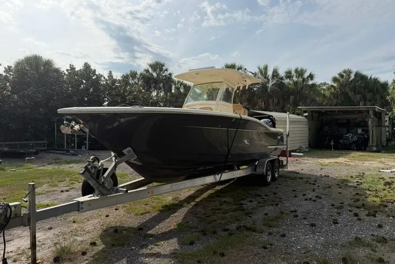 Slide: The Image of 2019 Scout 275 LXF boat on trailer, parked outdoors with trees in background. - 2