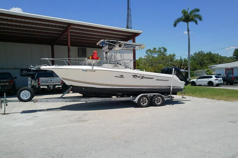 The Image of 2003 Wellcraft 250 Fisherman boat on trailer, parked outdoors under a metal canopy. - 0