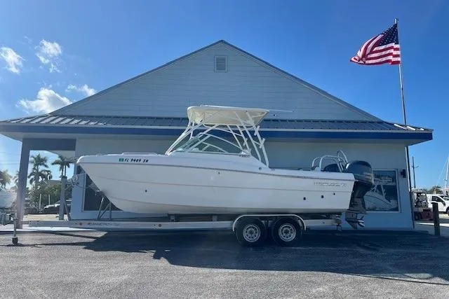 The Image of 2020 World Cat 230 DC boat on trailer, parked by a building with an American flag. - 1