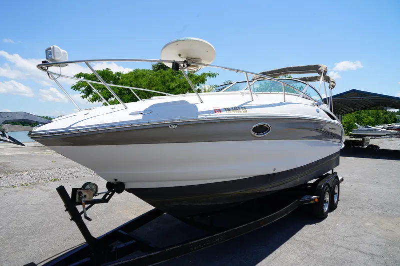 The Image of 2004 Crownline 250 CR boat on trailer, parked outdoors under clear blue sky. - 0