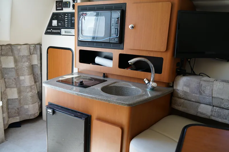 Slide: The Image of 2004 Crownline 250 CR boat interior with kitchenette, microwave, sink, and seating area. - 18