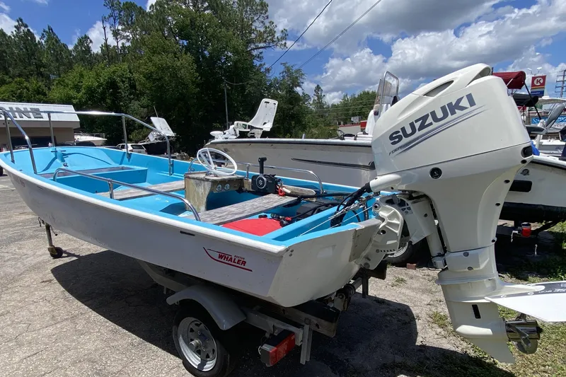 Slide: The Image of 1959 Boston Whaler 13 boat with Suzuki outboard motor, parked outdoors on a trailer. - 2