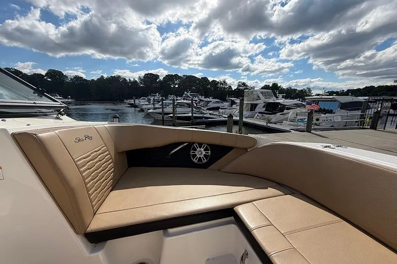 Slide: The Image of 2021 Sea Ray SPX 210 boat interior with tan seating, docked at a marina under a cloudy sky. - 23