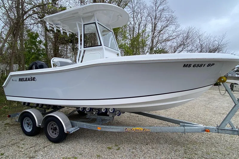 The Image of 2021 Release 210 RX boat on trailer, parked outdoors, surrounded by trees. - 0