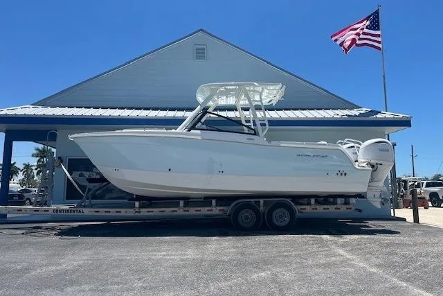 The Image of 2026 World Cat 265 DC-X boat on trailer, parked outside building with American flag. - 1