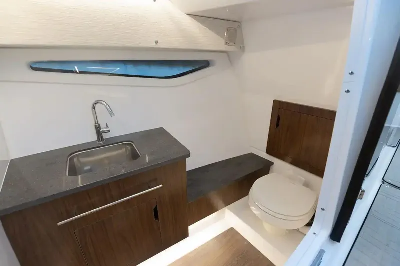 Slide: The Image of Manufacturer Provided Image: 2026 Four Winns H33 OB boat interior bathroom with sink, toilet, and wooden cabinetry. - 8