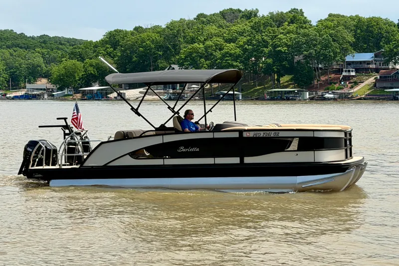 Slide: The Image of 2023 Barletta Lusso 23U pontoon boat cruising on a lake with lush green shoreline. - 5
