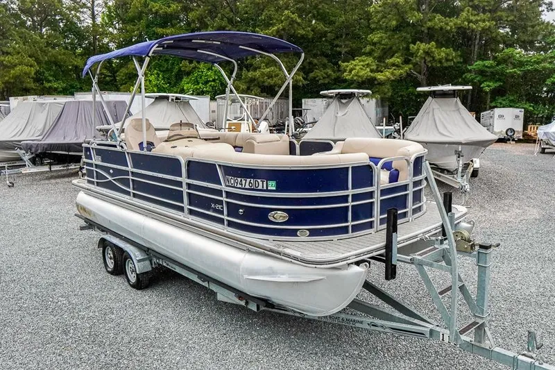 The Image of 2012 Xcursion X21C pontoon boat on trailer in outdoor storage area. - 1
