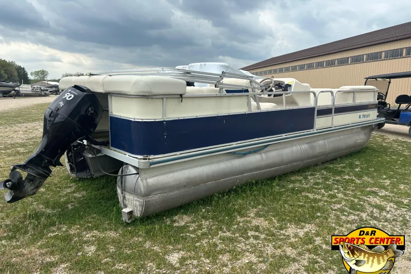 Slide: The Image of 2002 Odyssey Pontoons 2303L boat with outboard motor on grassy area near storage facility. - 2