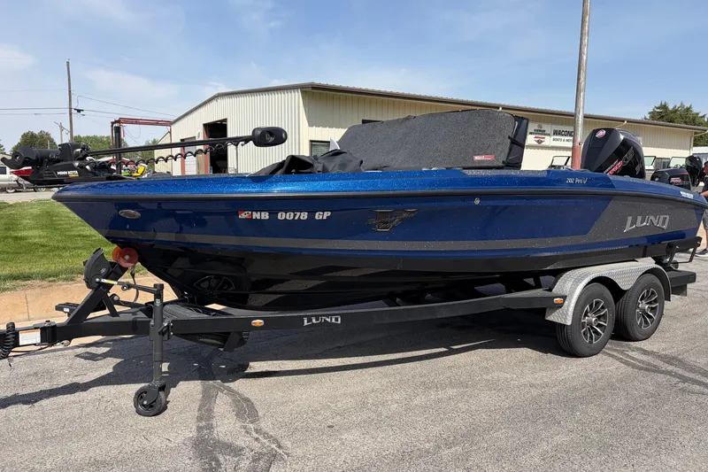 The Image of 2024 Lund 202 Pro-V GL boat on trailer, parked outdoors near a building. - 1
