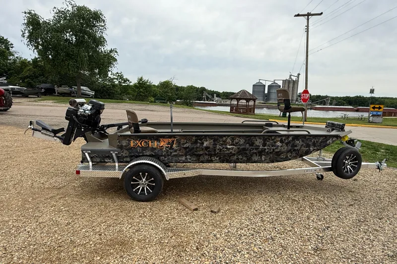 The Image of 2026 Excel 1860 Shallow Water F4 boat on trailer, camo design, parked outdoors. - 0