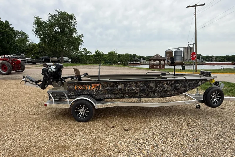 Slide: The Image of 2026 Excel 1860 Shallow Water F4 boat on trailer, parked near a lake. - 2