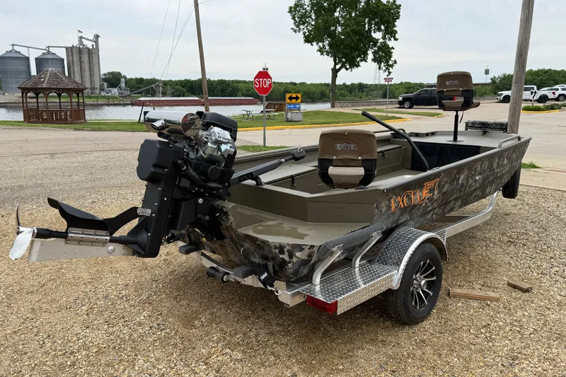 Slide: The Image of 2026 Excel 1860 Shallow Water F4 boat on trailer, parked near a river with industrial background. - 4