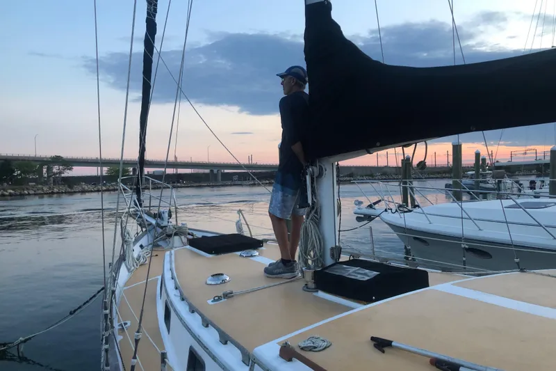 Slide: The Image of Man standing on 1979 Downeast DE38 sailboat at sunset, near a bridge. - 4