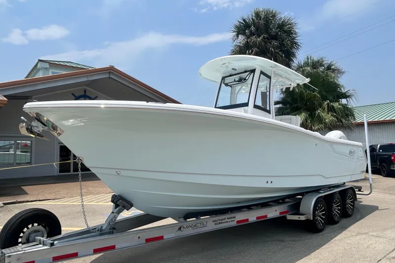 Slide: The Image of 2026 Sea Hunt Gamefish 27 Coffin Box boat on trailer, parked outdoors near palm trees. - 1