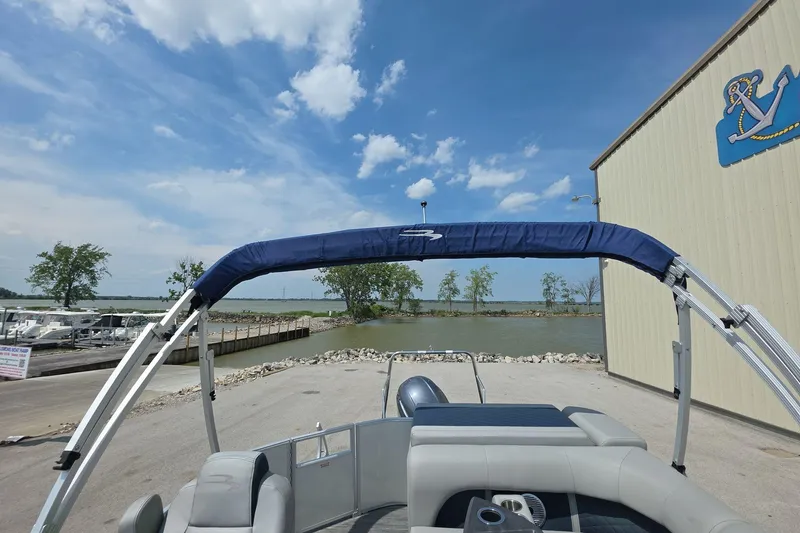 Slide: The Image of 2022 Bennington L 21 L-Bench pontoon boat docked by a serene waterfront. - 4