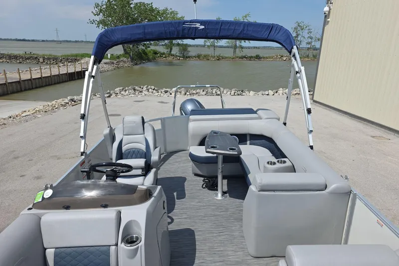 Slide: The Image of 2022 Bennington L 21 L-Bench pontoon boat with spacious seating and canopy, docked by a lake. - 9
