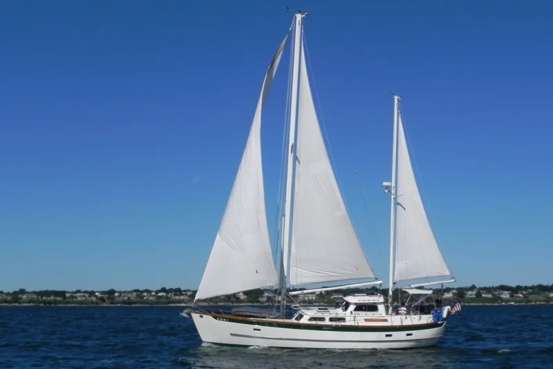 The Image of A 1980 Cheoy Lee 43 Pilot House yacht sails on calm waters under a clear sky. - 0