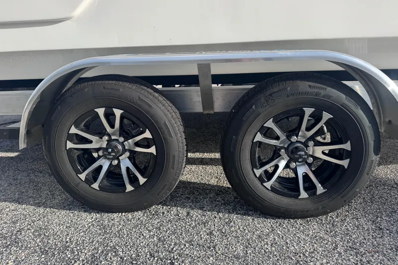 Slide: The Image of 2026 Sundance B22CCR trailer wheels on gravel, featuring sleek black and silver rims. - 13