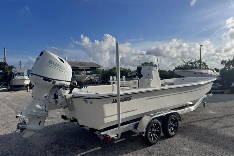 Slide: The Image of 2026 Sundance B22CCR boat with Suzuki outboard motor on a trailer, parked outdoors. - 2