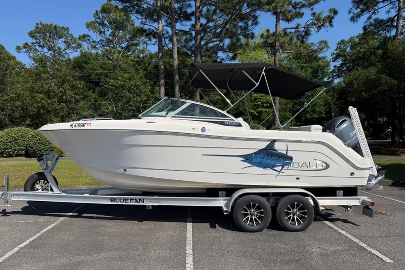 The Image of 2015 Robalo R227 Dual Console boat on trailer, parked outdoors with trees in background. - 1