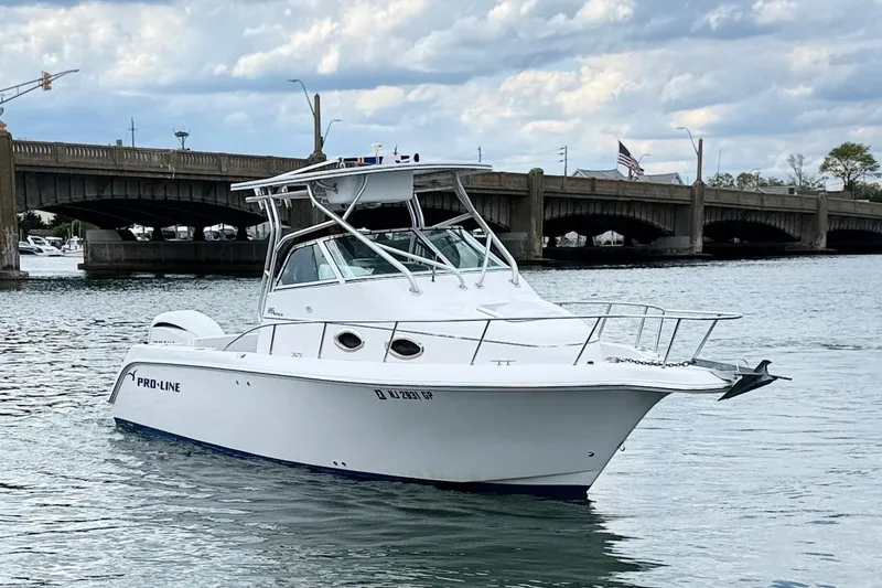 Slide: The Image of 2001 Pro-Line 260 Walkaround boat on water near a bridge under cloudy skies. - 2
