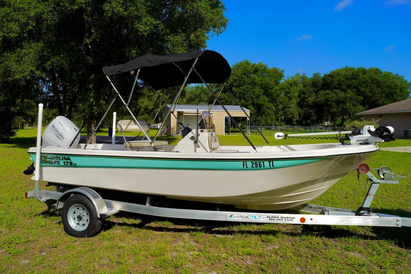 Slide: The Image of 2023 Carolina Skiff 178 JLS boat on trailer, parked on grass with trees in background. - 2