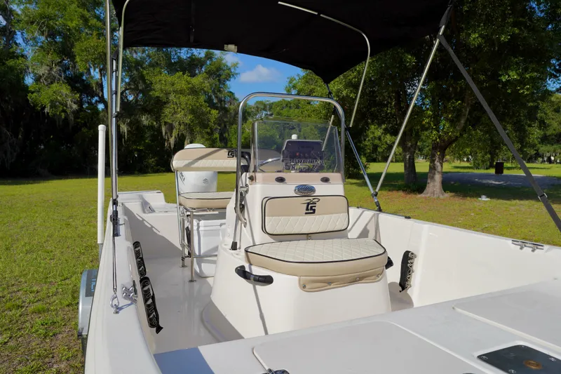 Slide: The Image of 2023 Carolina Skiff 178 JLS boat interior with seating and console, set in a grassy area. - 5