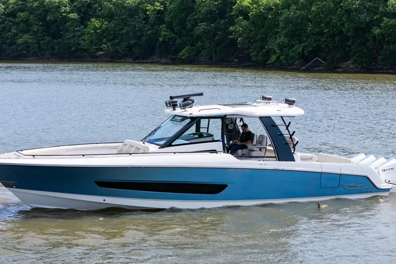 Slide: The Image of 2021 Boston Whaler 420 Outrage boat cruising on a serene lake with lush green trees. - 38
