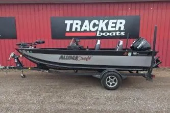 The Image of 2022 Alumacraft Competitor 165 SC fishing boat on trailer, parked by Tracker Boats sign. - 1